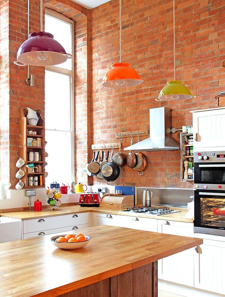 The brick wall backdrop with sleek colander lights diverts the focus away from the small size of the kitchen .